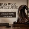 A dark wood carved wave sculpture resting on a wooden base atop a table alongside Kinfolk books. Overlay text reads: "DARK WOOD WAVE SCULPTURE", "Drama and Beauty in One Piece:", and a dark badge stating "7 WAYS THIS OCEANIC MASTERPIECE ELEVATES YOUR INTERIOR". In the background, a minimalist framed landscape painting and small potted plant adorn a cozy room set. The website "TIMBERBLOOM.COM" is displayed at the bottom.