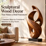 A horizontal graphic titled "Sculptural Wood Decor That Makes a Bold Statement: 7 Fearless Ways to Command Attention in Any Room". The image features a large, flowing, abstract wooden loop sculpture displayed on a black plinth inside a sunlit living room. Warm natural light filters in across a beige sofa, round coffee table, and wooden bookshelf. A button highlights the website woodzaa.com.